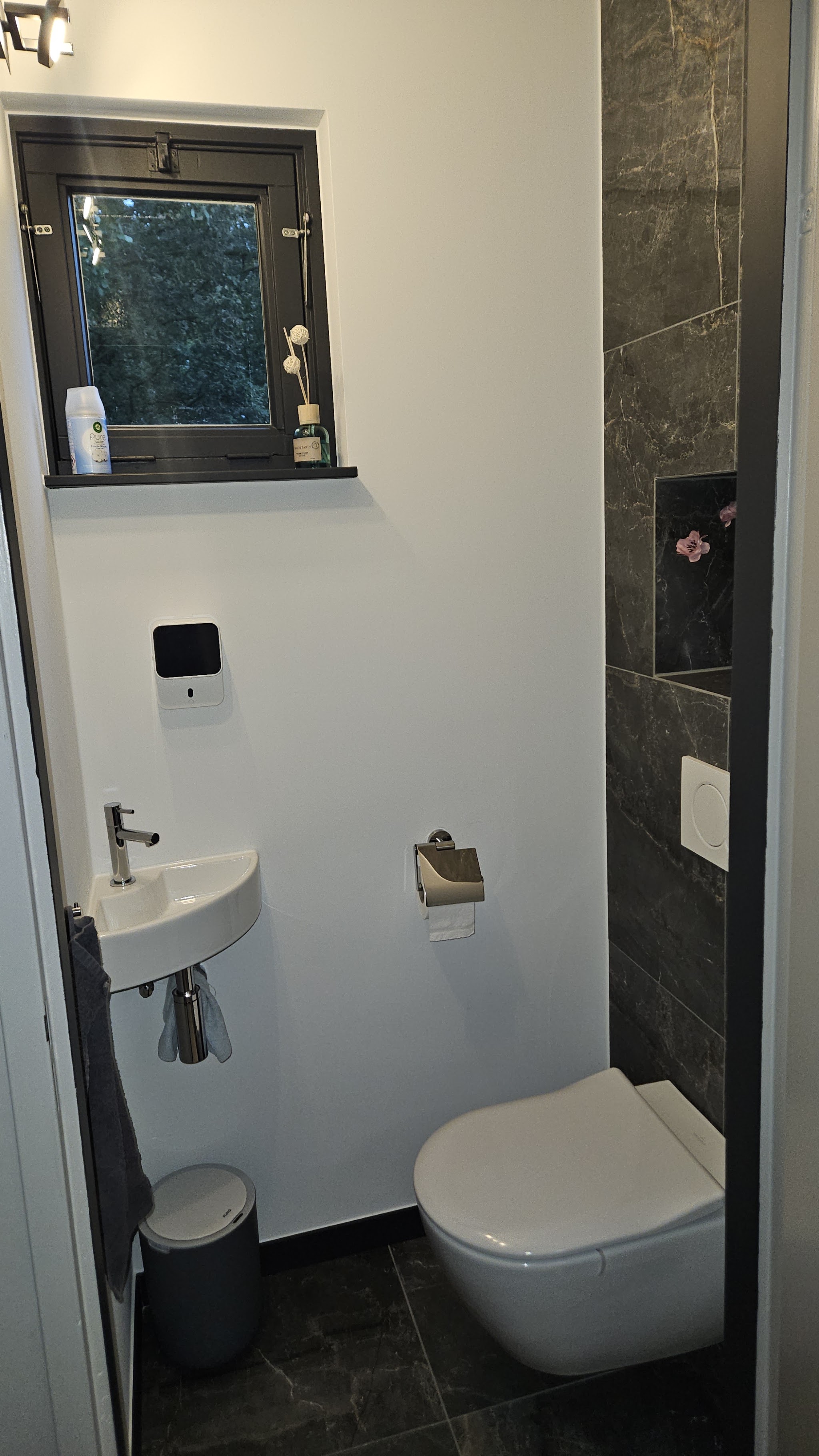 Het vernieuwde toilet: wit hangtoilet, fontein, raam met zwart kozijn en een tegelwand in marmerlook
