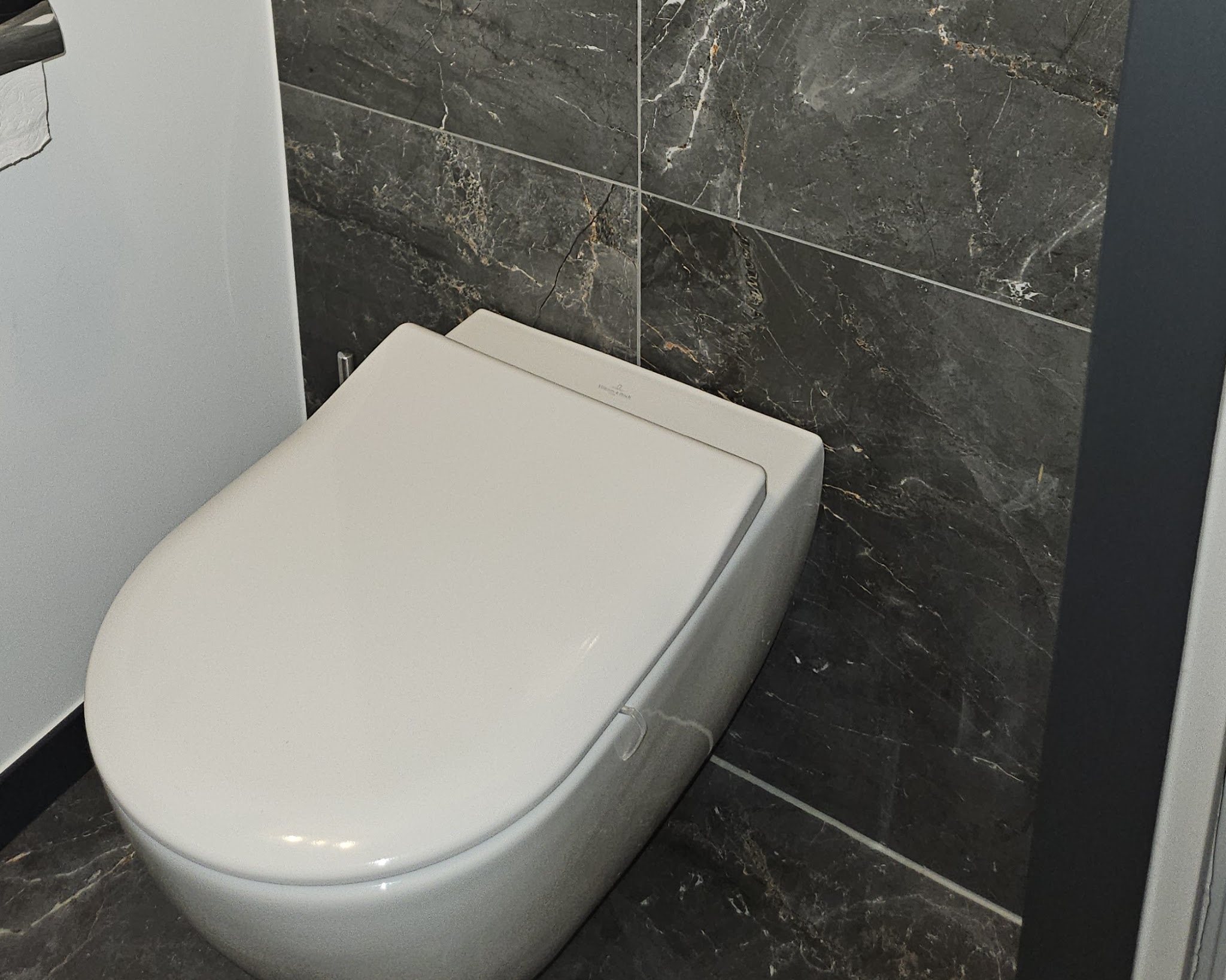 Hangtoilet tegen een wand van donkere marmerlook tegels, gerenoveerd door JKW Installaties